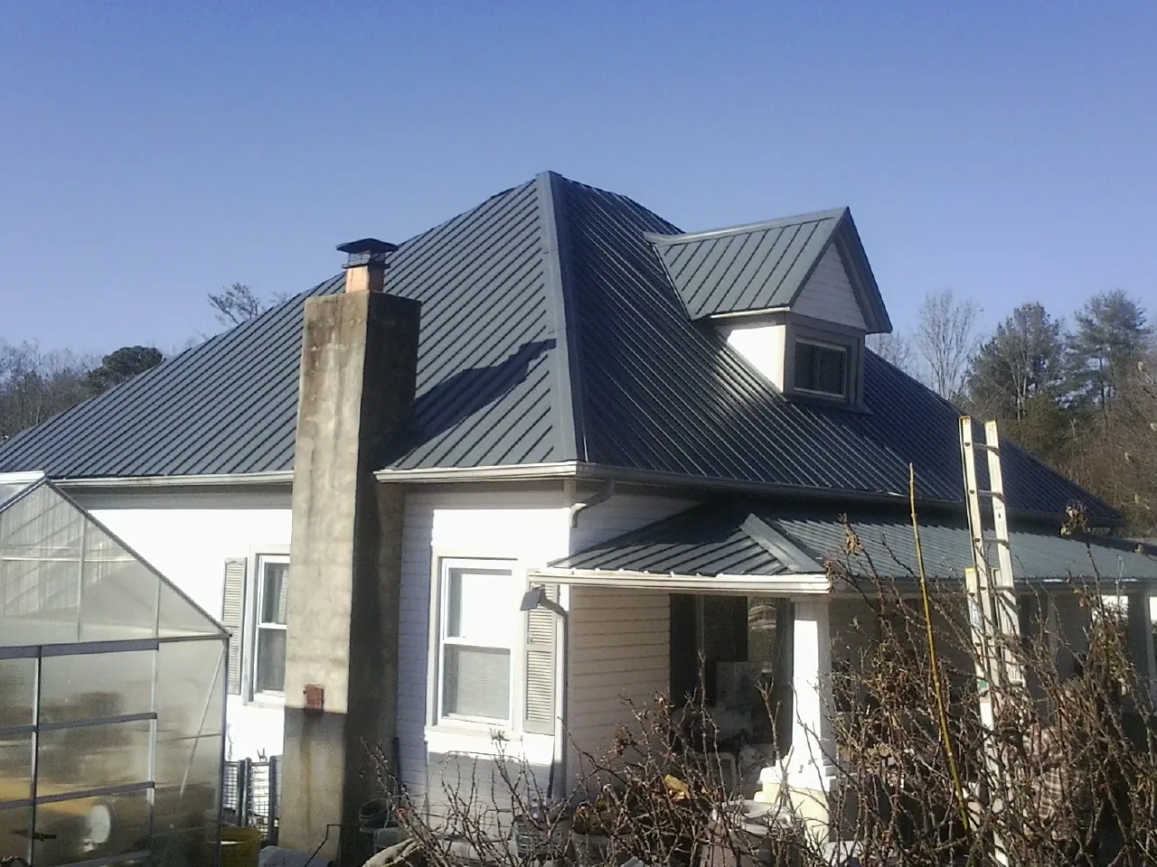 Dark blue standing seam metal roof on a white farmhouse with dormer — Slate & Tile Roof Repair by Roofing Brothers in Prairie