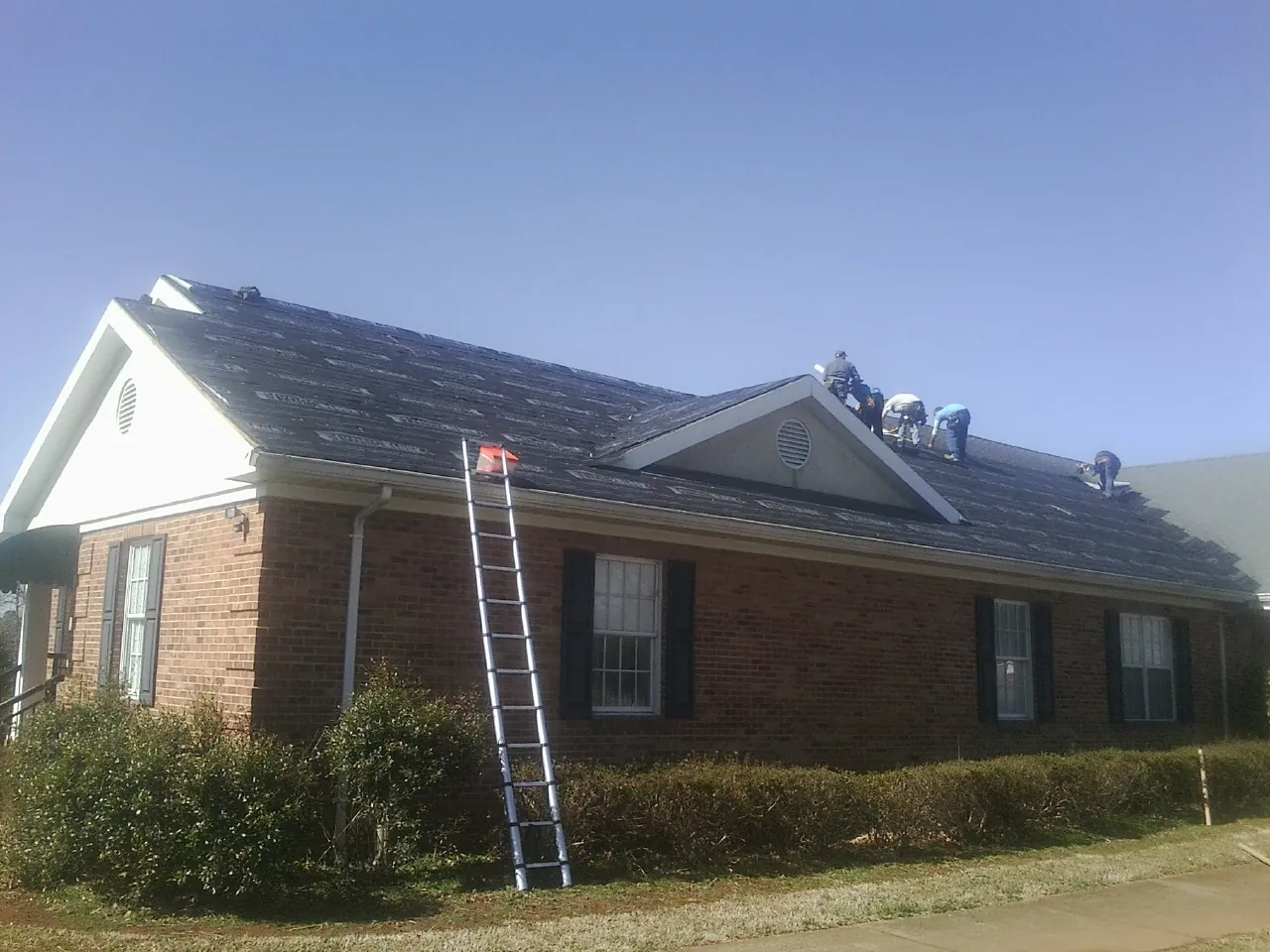 Crew tearing shingles off a brick ranch roof with a ladder set — Emergency Roof Repair work by our crew in Prairie