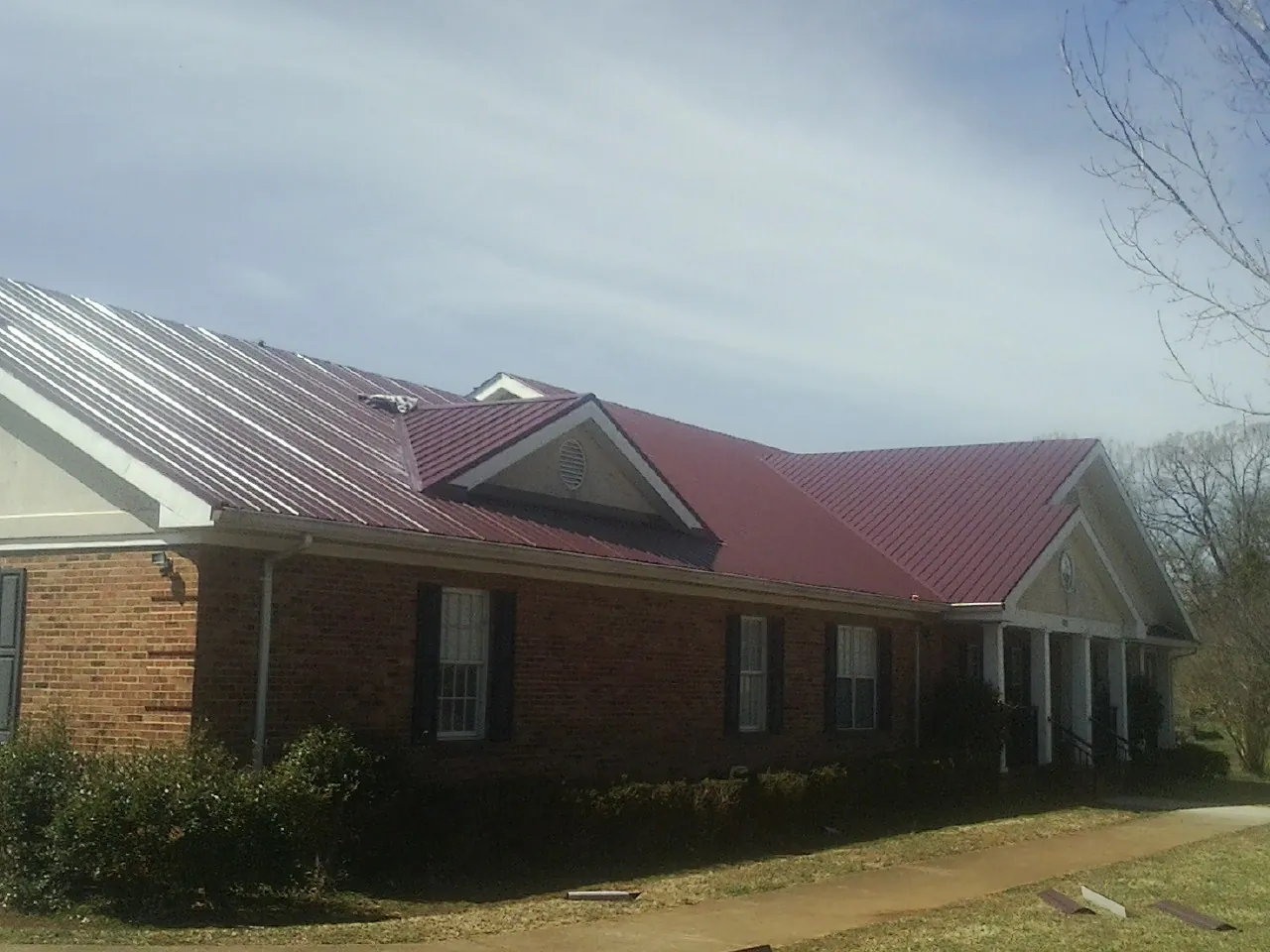 Red metal roof with gabled entries on a long brick building, from a Hail Damage Roof Repair job in Prairie