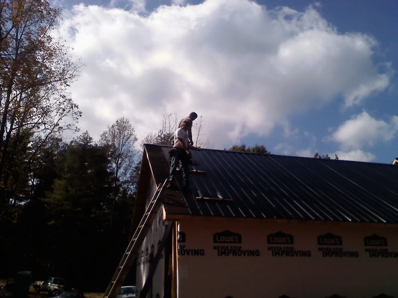 Roofer fastening dark metal panels high against a cloudy sky, from a Roof Inspection job in Prairie