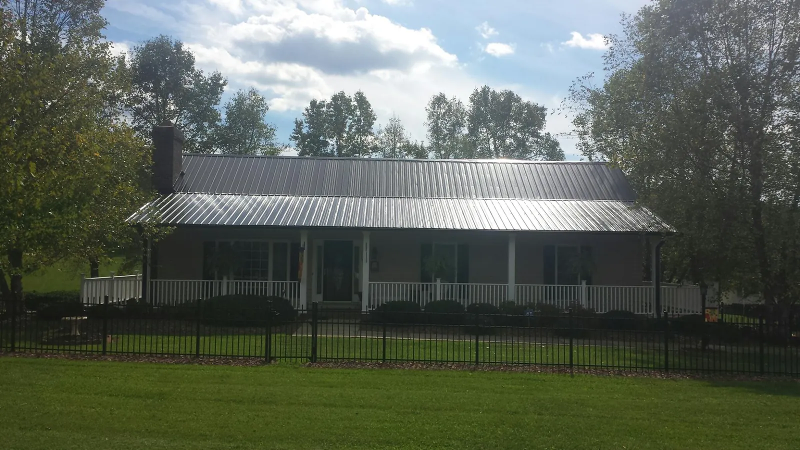 Gray metal roof on a brick ranch with a full width front porch — Gutter Guard Installation work by our crew in Prairie