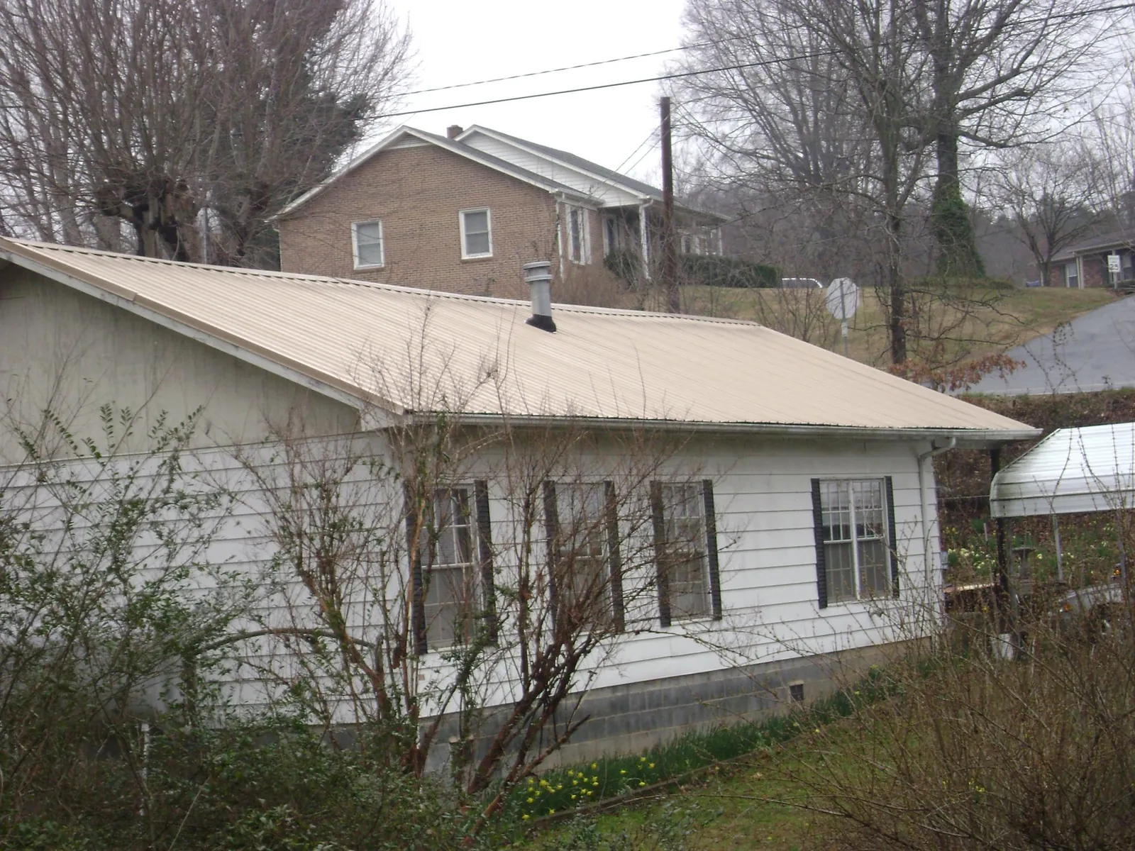 Tan metal roof on a white sided house set into a hillside — Commercial Roofing by Roofing Brothers in Prairie