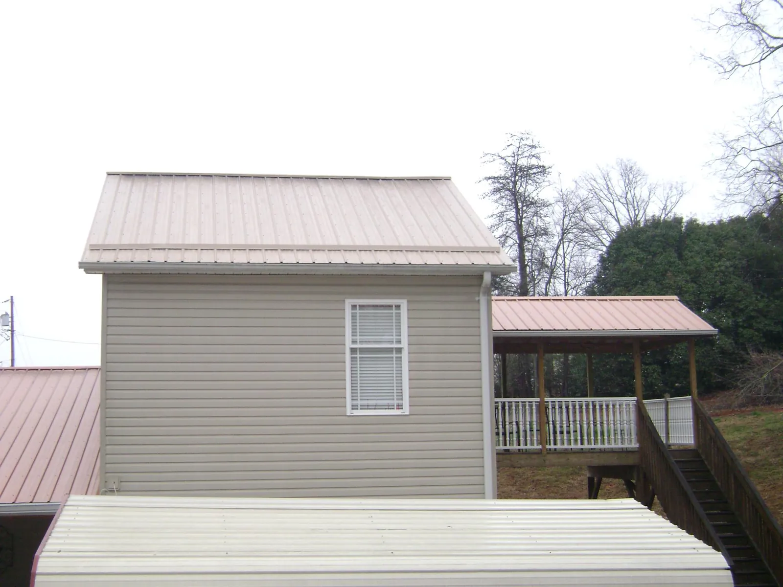 Tan metal roofs on a two story addition and attached porch, from a Roof Replacement job in Prairie